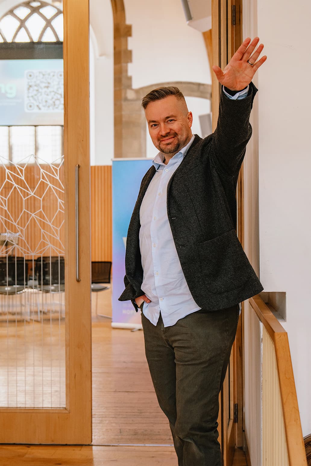 A smiling pastor waving hello at the door of the church hall